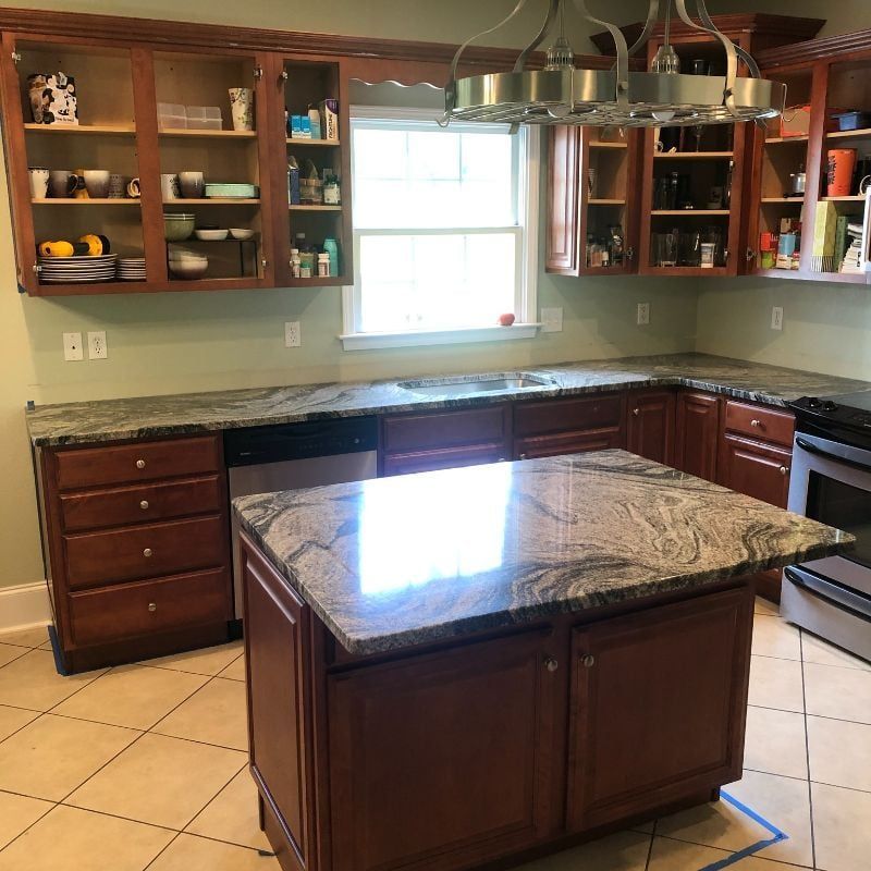 Empty kitchen with dark wood cabinets, granite countertops, and a large island under a window.