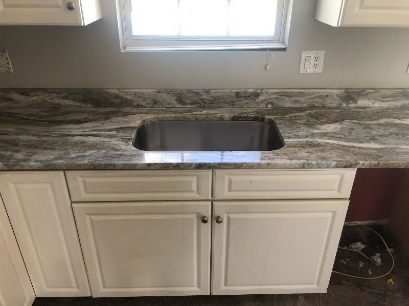 Kitchen sink beneath a window with white cabinets and dark stone countertop
