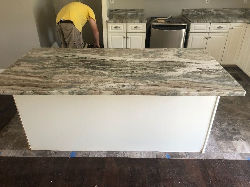 Kitchen island with granite countertop being installed, with a worker bending over in the background