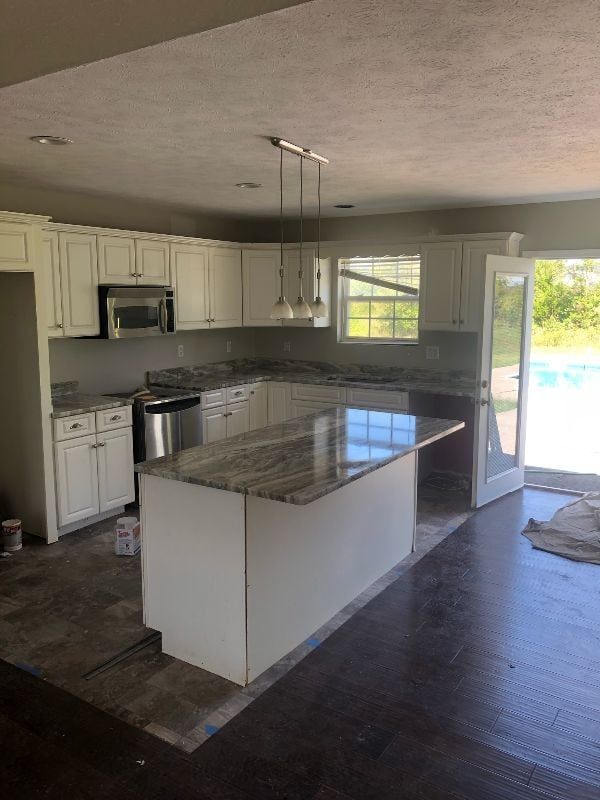 Empty kitchen with white cabinets, granite island, and open glass door to outside.