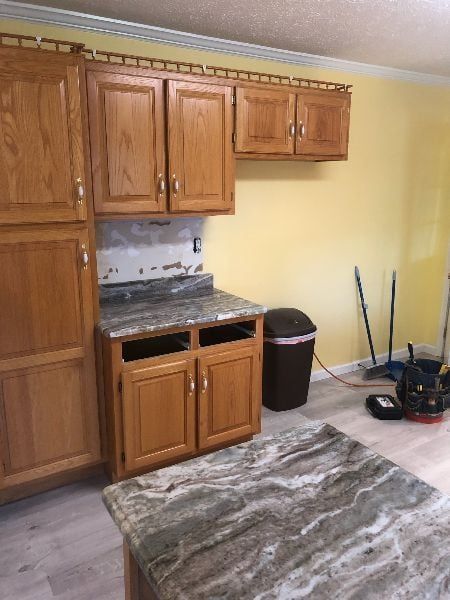 Small kitchen with wooden cabinets, granite counters, yellow walls, and a patterned rug on the floor.