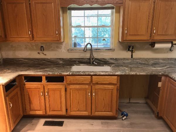 Wooden kitchen with granite countertops, sink under window, and empty lower cabinet openings under the counter.