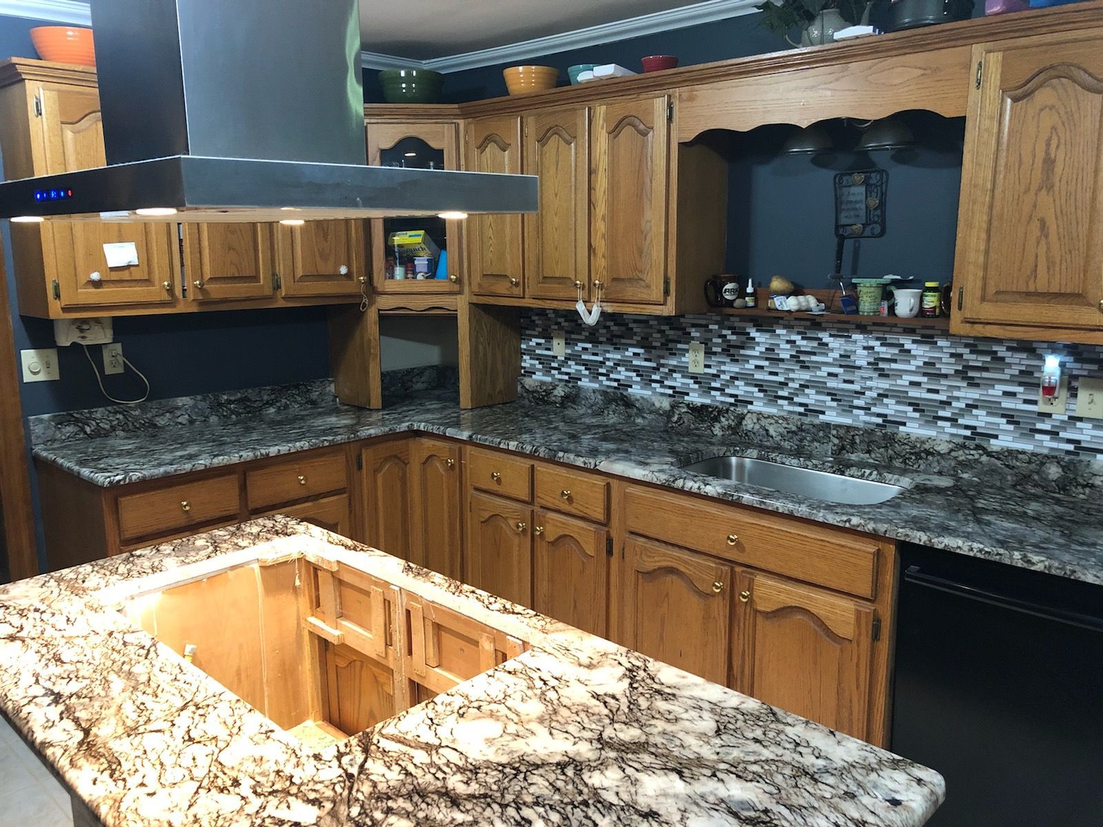 Kitchen under renovation with granite countertops, wooden cabinets, and a central island opening in the floor