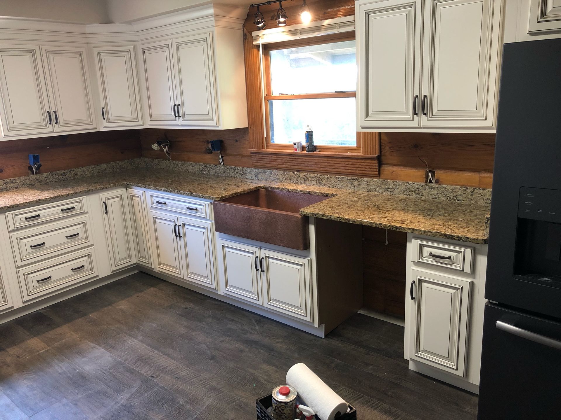 White kitchen with granite countertops, stained cabinets, window above sink, and black refrigerator