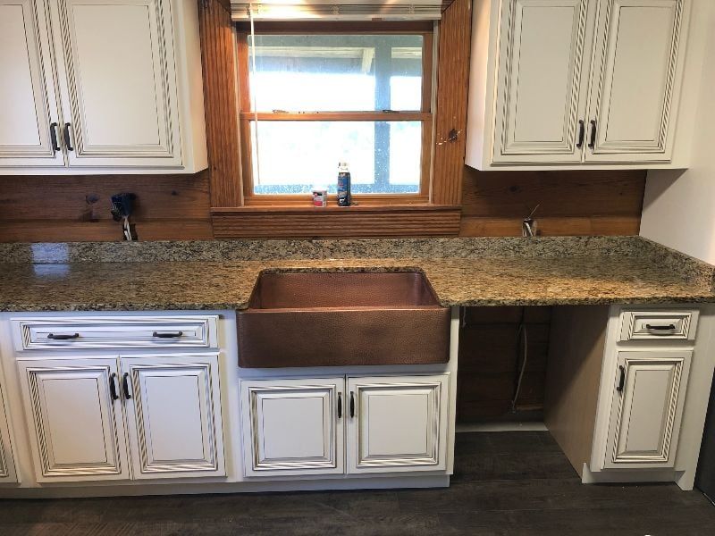 Kitchen sink under window with white cabinets and granite countertop