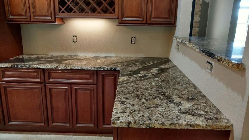 Kitchen with dark wood cabinets and speckled granite countertops, including a peninsula by a window.