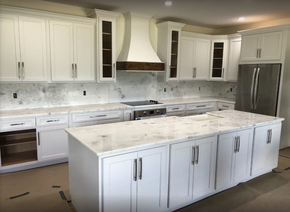 Bright white kitchen with marble island, white cabinets, stainless appliances, and gray backsplash.