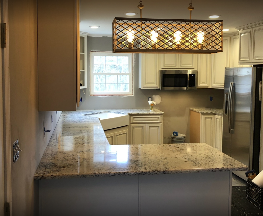 Modern kitchen with granite island, white cabinets, stainless appliances, and hanging light fixture