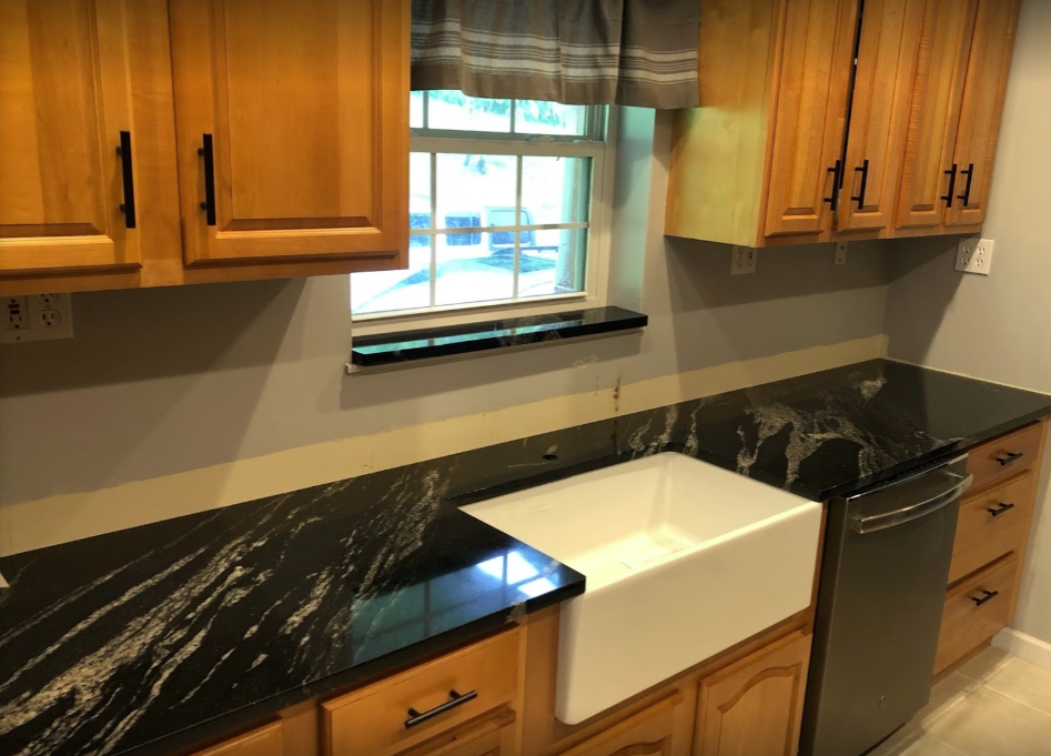 Kitchen countertop with black granite, wooden cabinets, and a white sink under a window