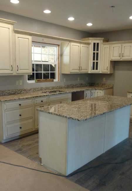 Empty modern kitchen with cream cabinets, granite counters, and a central island under recessed lights