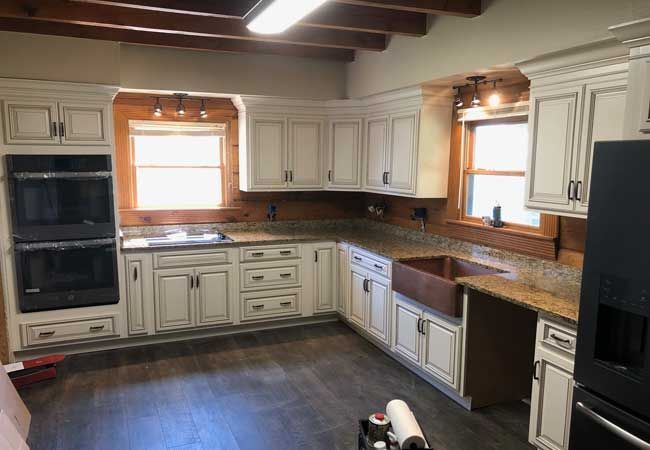 Bright kitchen with white cabinets, dark wood beams, and granite countertops by two windows.