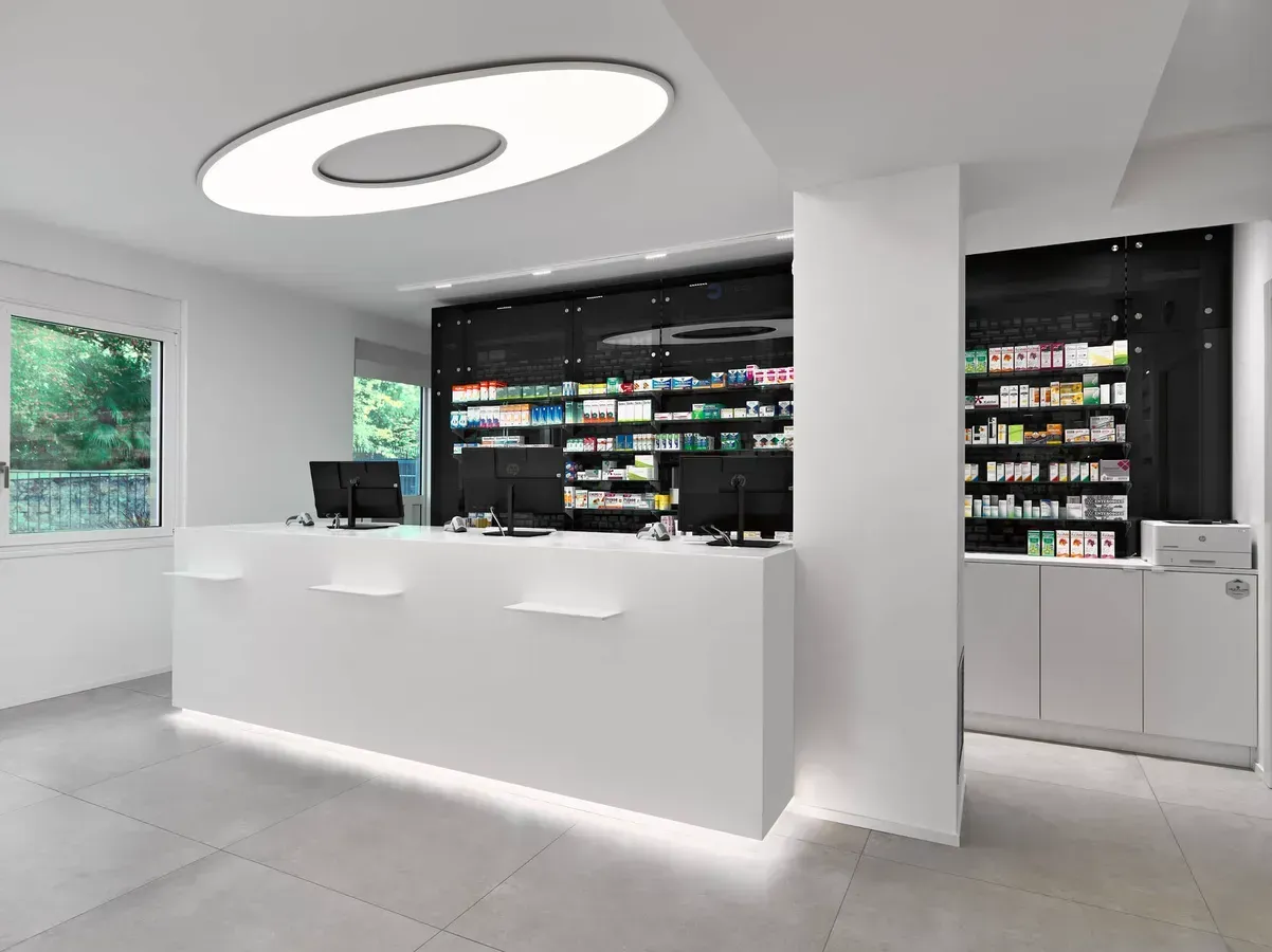 Arredamento Farmacia Passirani Lesa, lampada Elcom, progettata dalla light designer Bianca Tresoldi, sovrasta il banco cassa