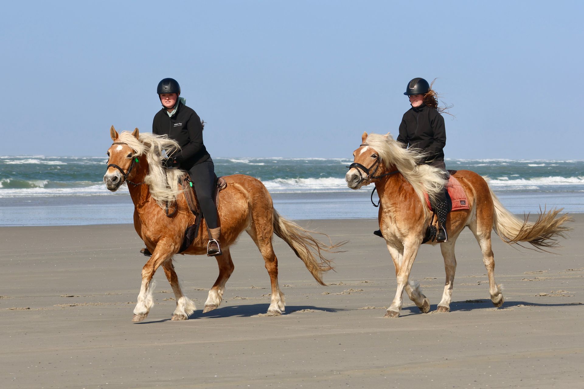 Two people are riding horses on the beach.