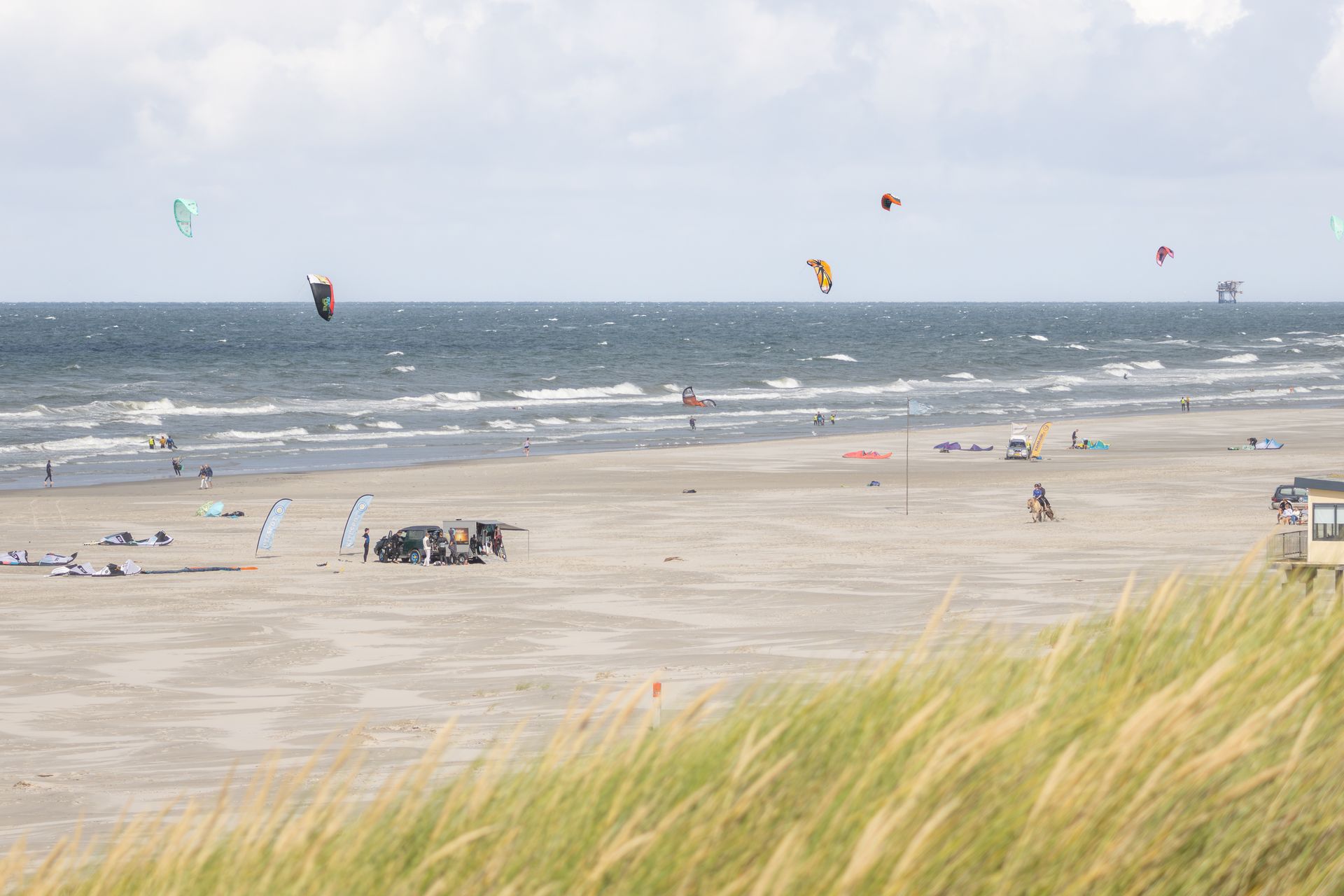 Strand met kitesurfers, bewolkte lucht, zand en oceaangolven.