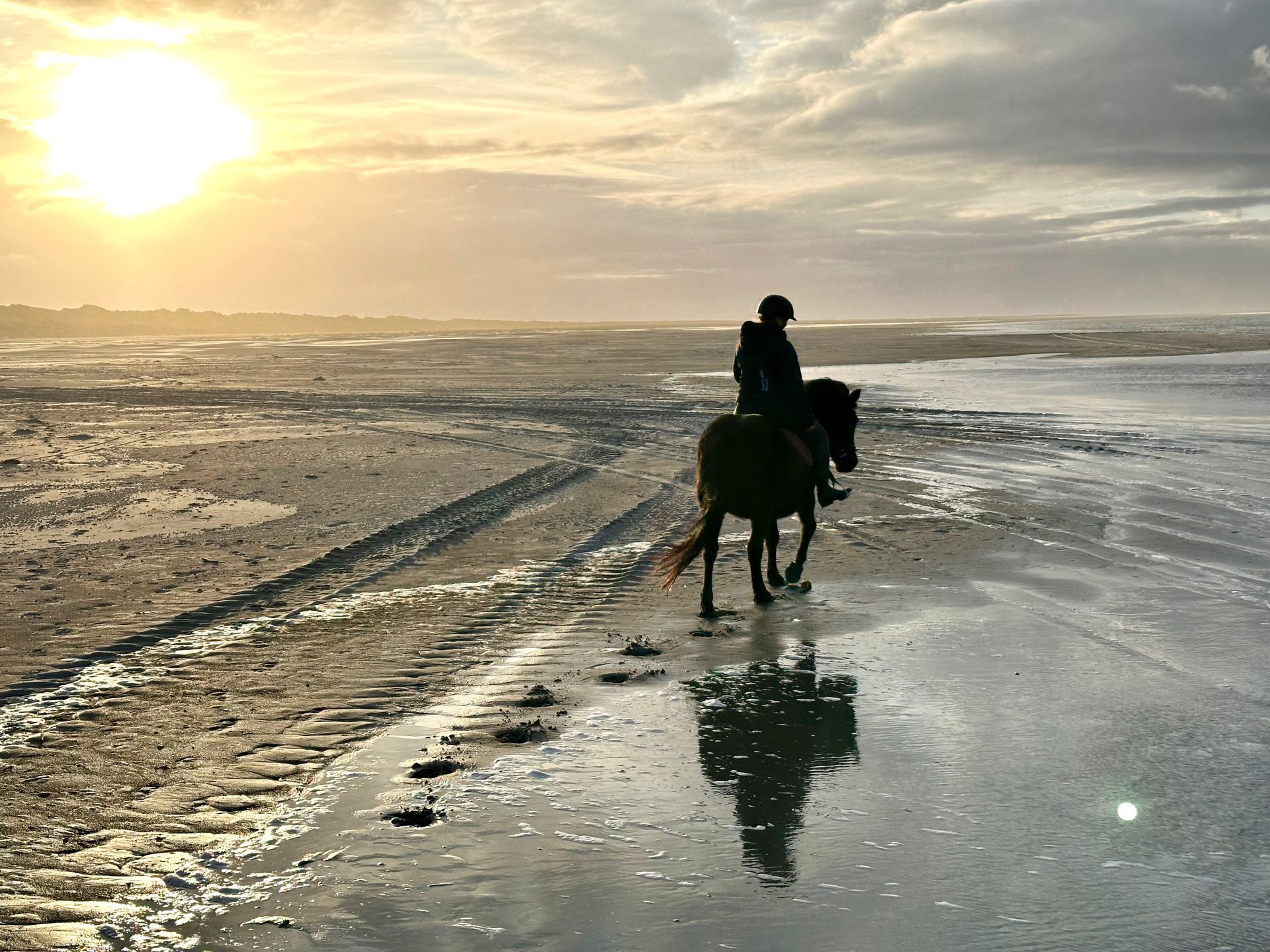 A person is riding a horse on the beach at sunset.