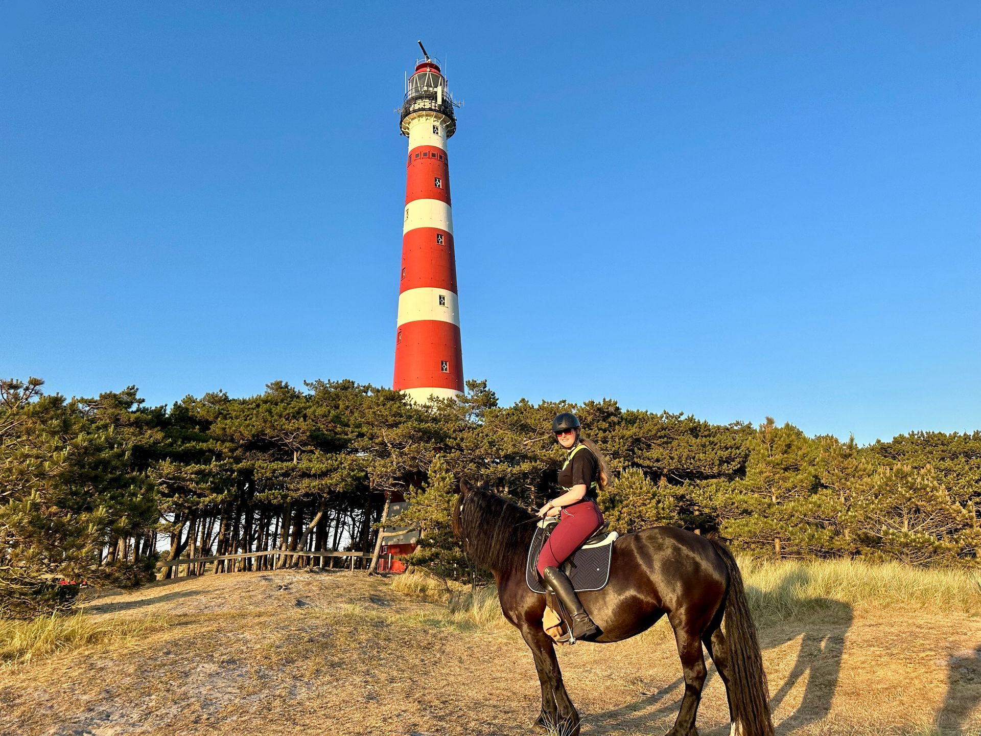 A person is riding a horse in front of a lighthouse.