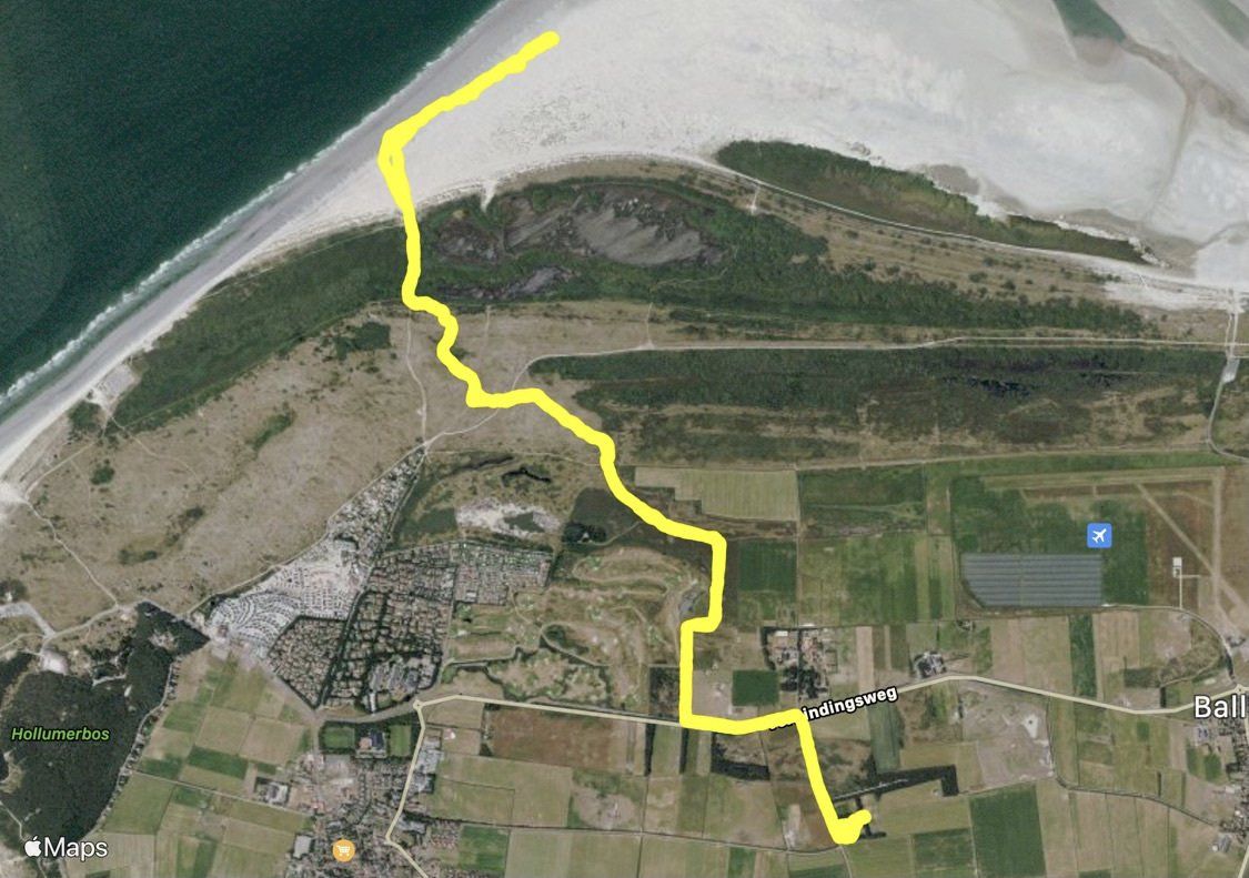 Luchtfoto van een geel pad dat door een kustlandschap met velden en strand slingert.