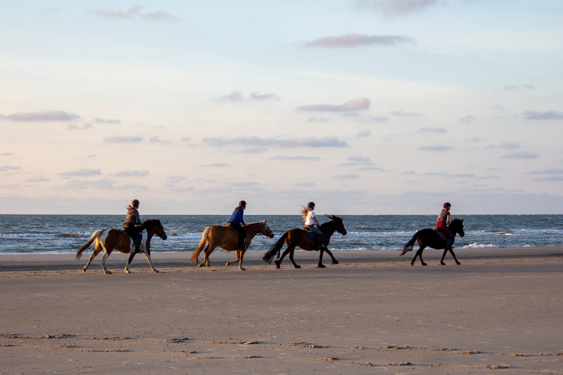 Gevorderde ruiters rijden tijdens zonsondergang over het strand van Ameland met zee op de achtergrond.