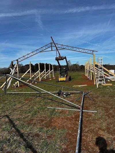 Construction site: Metal beams being lifted into place by a machine, wooden supports, blue sky.