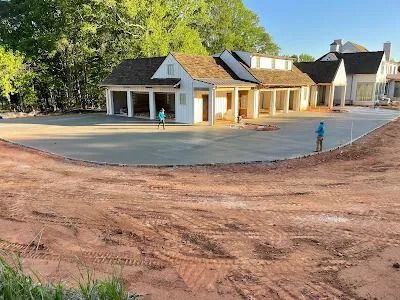 Newly poured concrete driveway with a house under construction; workers present.