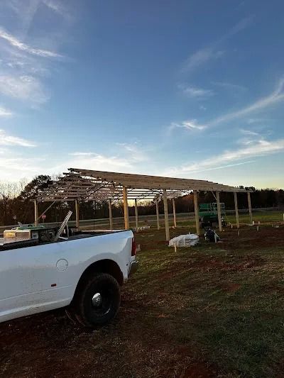 White truck parked near a wooden structure under construction in a field, blue sky overhead.