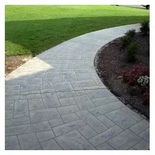 Curving gray stone pathway next to green lawn and a flowerbed with plants.