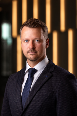Portrait of a man in a dark suit and tie against a blurred warm-lit background