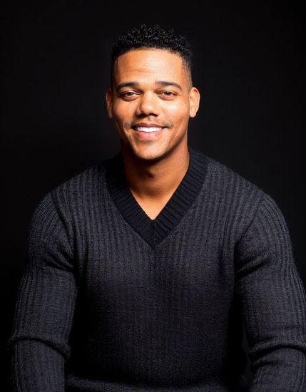 The man is wearing a black sweater and smiling for the camera.
