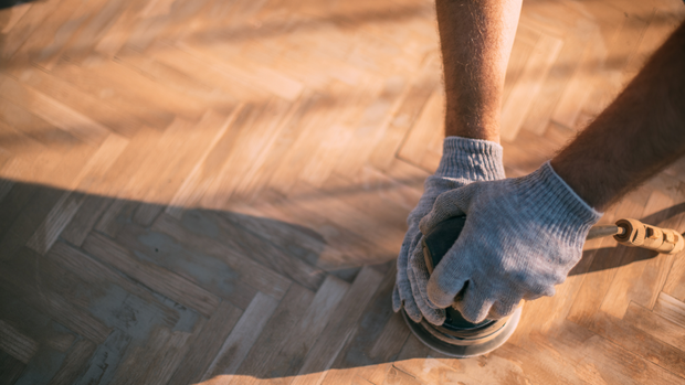 A person is sanding a wooden floor with a sander.
