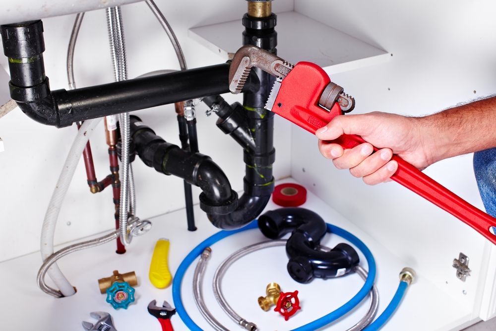 A Plumber Using a Red Wrench on Black Pipes Under a Sink — David Lewis Solahart in Tenterfield, NSW