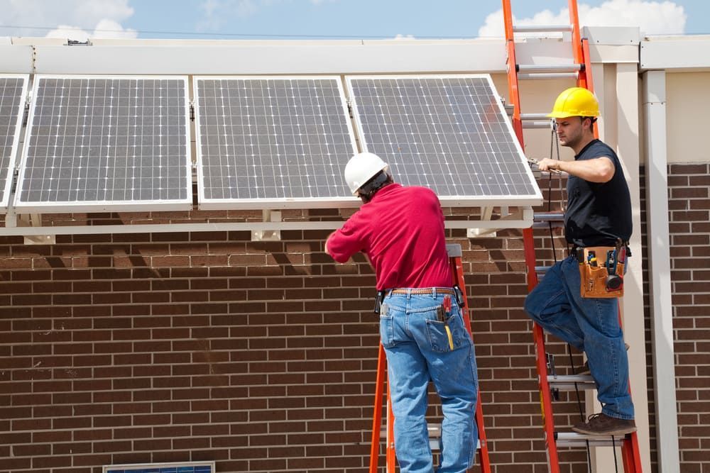 Two Men Are Installing Solar Panels On A Brick Building — David Lewis Solahart in Goonellabah, NSW