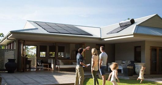 A Family Is Standing In Front Of A House With Solar Panels On The Roof