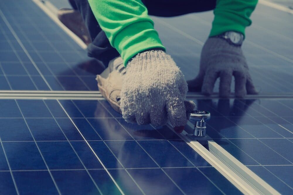 A Person is Installing Solar Panels on a Roof With Gray Gloves — David Lewis Solahart in Evans Head, NSW