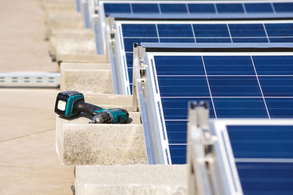 A Drill Is Sitting On A Concrete Surface Next To A Row Of Solar Panels — Solahart In Goonellabah, NSW