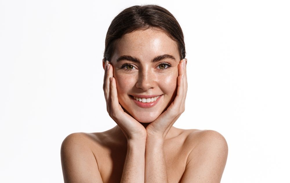 A smiling person with hands resting gently on their cheeks against a plain white background.