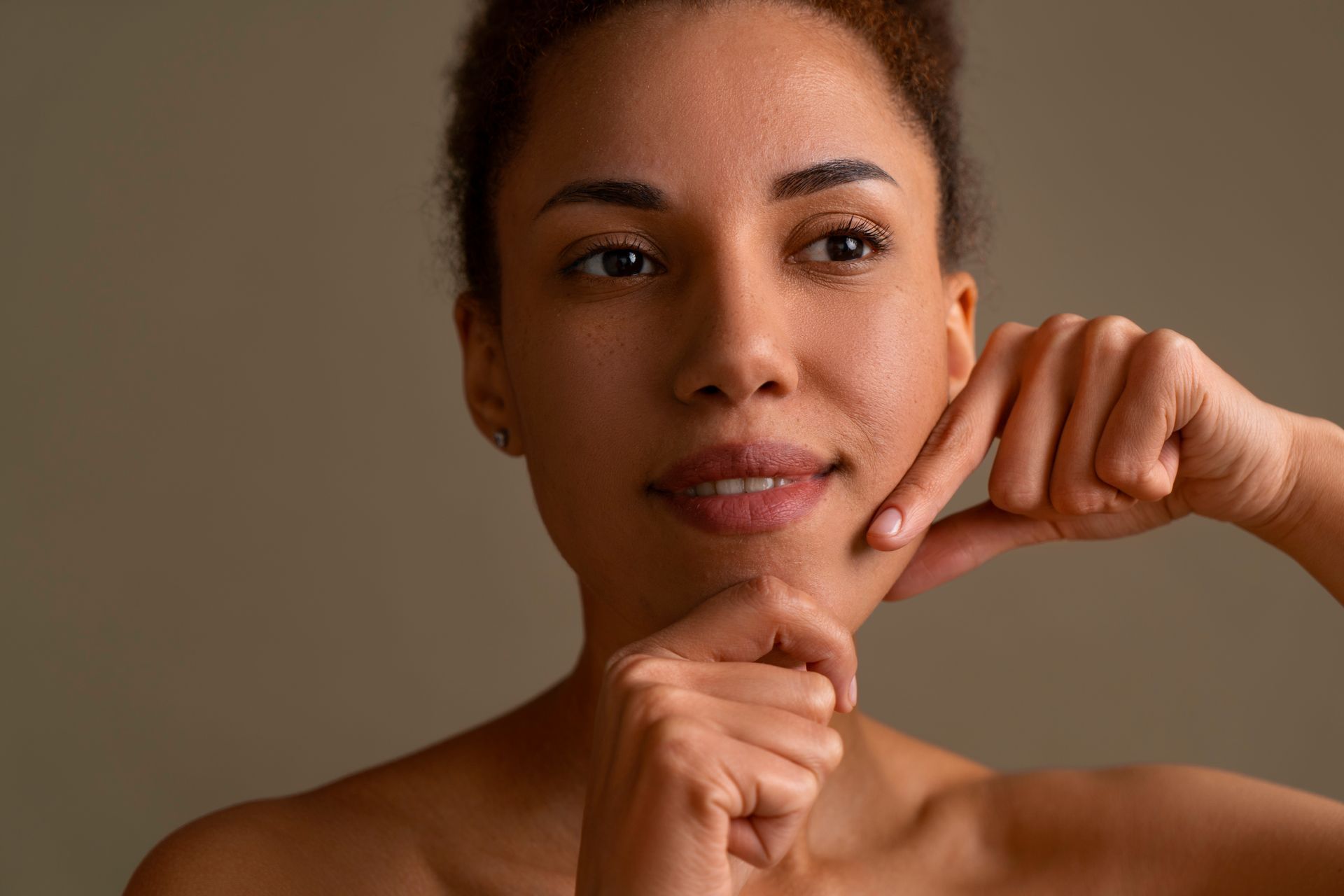 Close-up of a person posing with hands near the face against a plain brown background