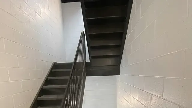 Stairwell with black metal railings and white cinderblock walls, viewed from the bottom looking up.
