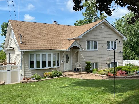 Suburban house with beige siding, brown roof, manicured lawn, and flower beds on a sunny day