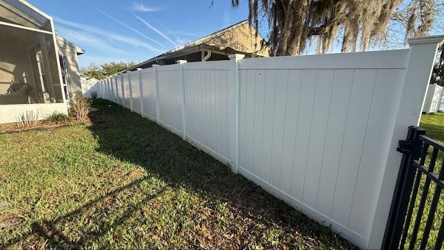 White vinyl privacy fence running along a grassy yard beside a house on a sunny day.