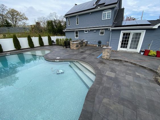 Backyard pool with gray stone patio and modern house, overcast sky