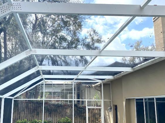 White metal patio roof frame under construction over a backyard deck, with blue sky and trees visible.