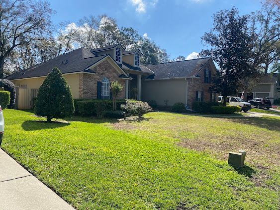 Single-story brick house with a large green front lawn and trees under a sunny blue sky