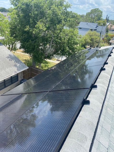 Solar panels covering a sloped rooftop beside trees and neighboring houses