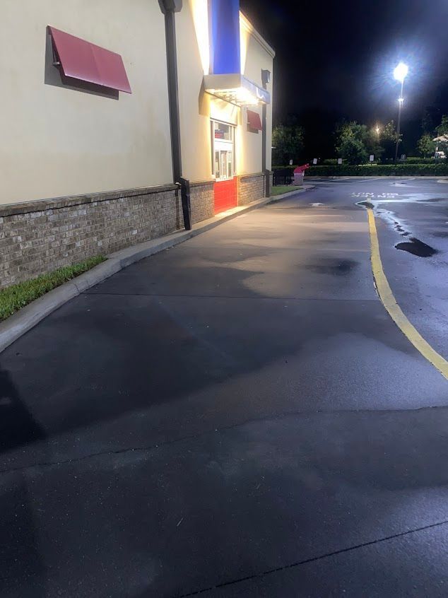Nighttime storefront with lit entrance, empty sidewalk, and wet pavement by a curved drive lane
