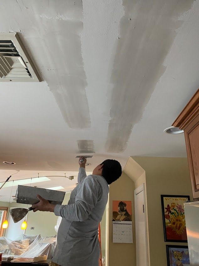 Person painting white patches on a ceiling in a room with framed wall art and hanging lights