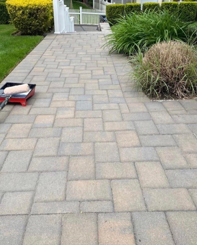Paver walkway beside shrubs, with a small red tool on the left and a gate in the distance.