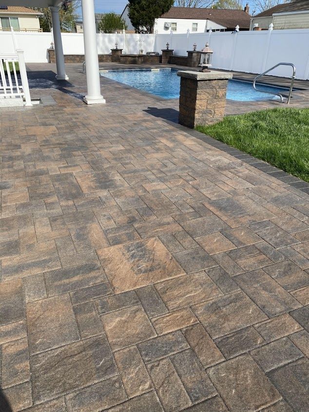 Patio pavers beside a swimming pool with white columns and a small patch of grass.