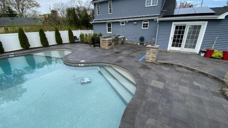 Backyard pool with curved stone deck beside a gray house and patio doors