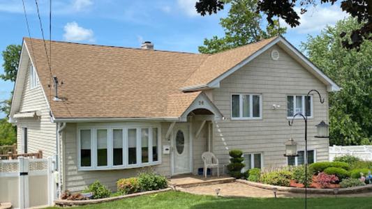 Single-story beige house with tan roof, white trim, front porch, and landscaped yard under a blue sky