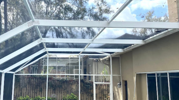 Screened patio with a white metal frame and translucent roof panels beside a house and trees